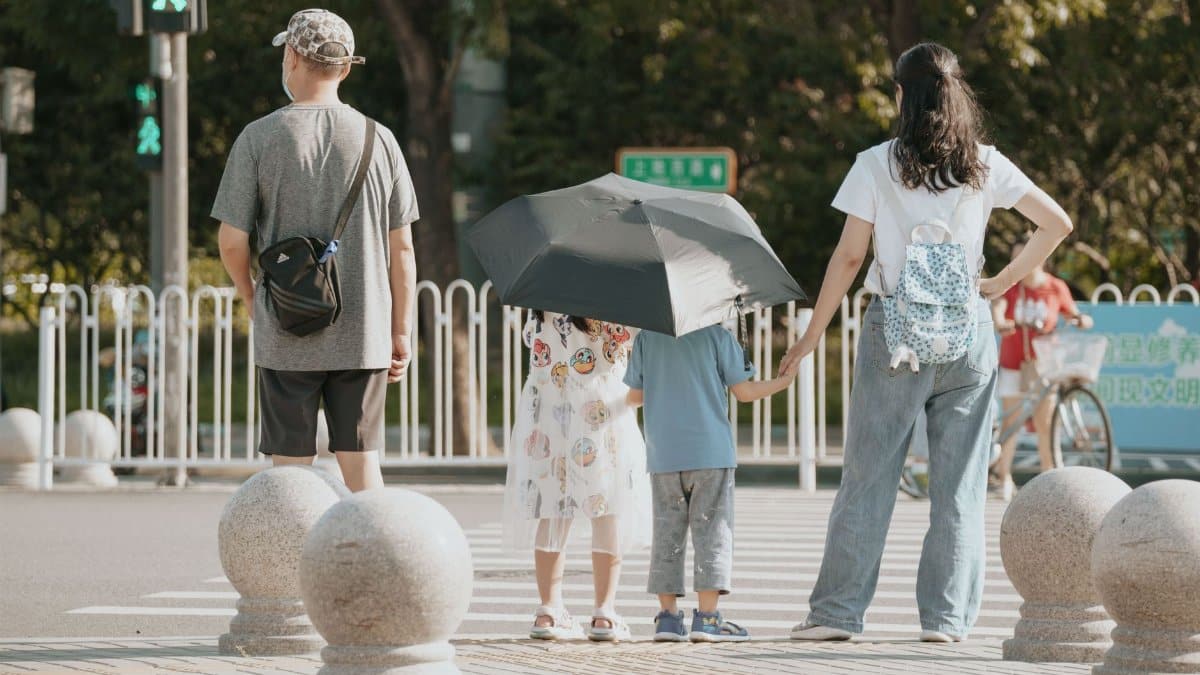 A family waits at a crosswalk with children holding an umbrella on a sunny day.