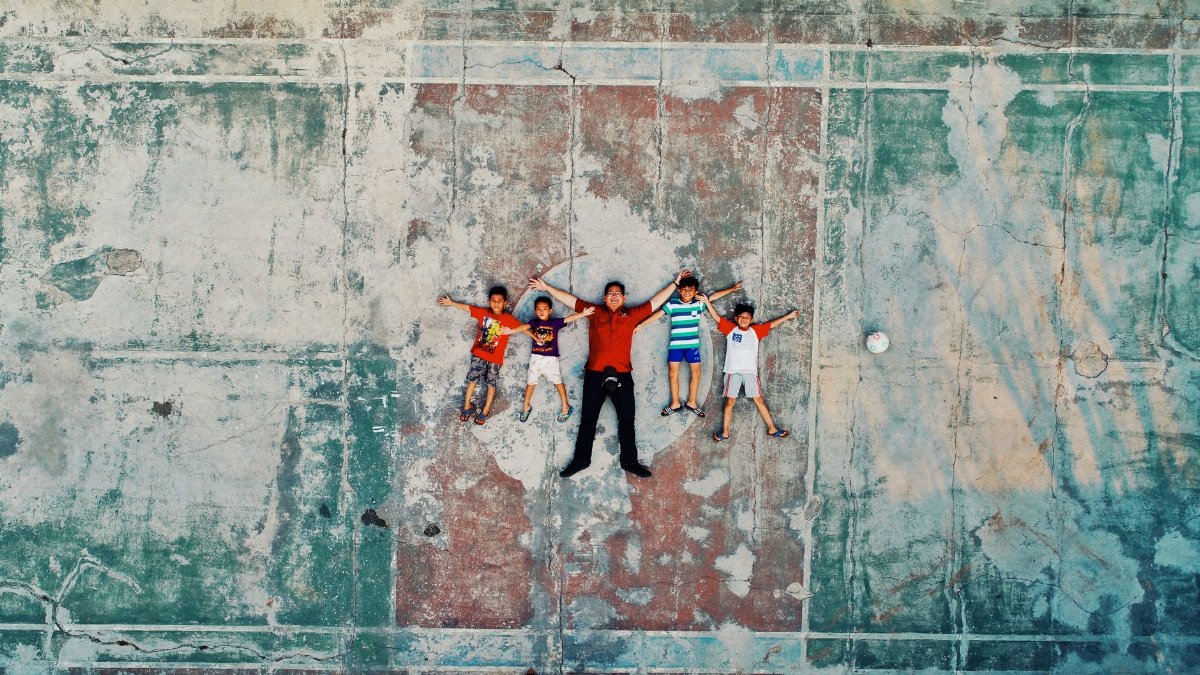 A family relaxes on a vintage basketball court in Medan, Indonesia, captured from above.