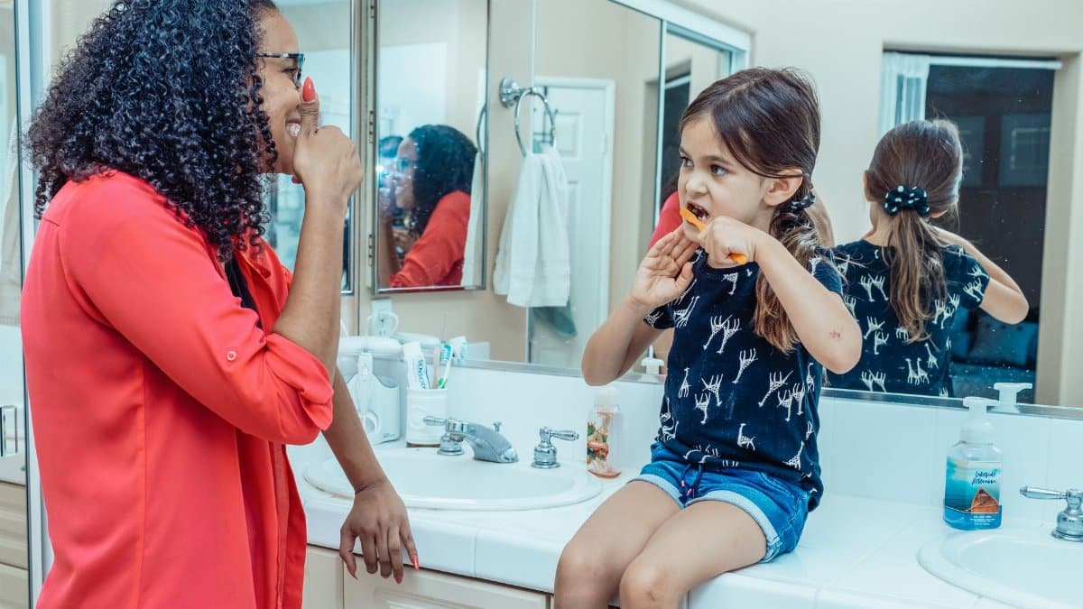 A mother teaches her daughter dental hygiene as they brush their teeth together in the bathroom.