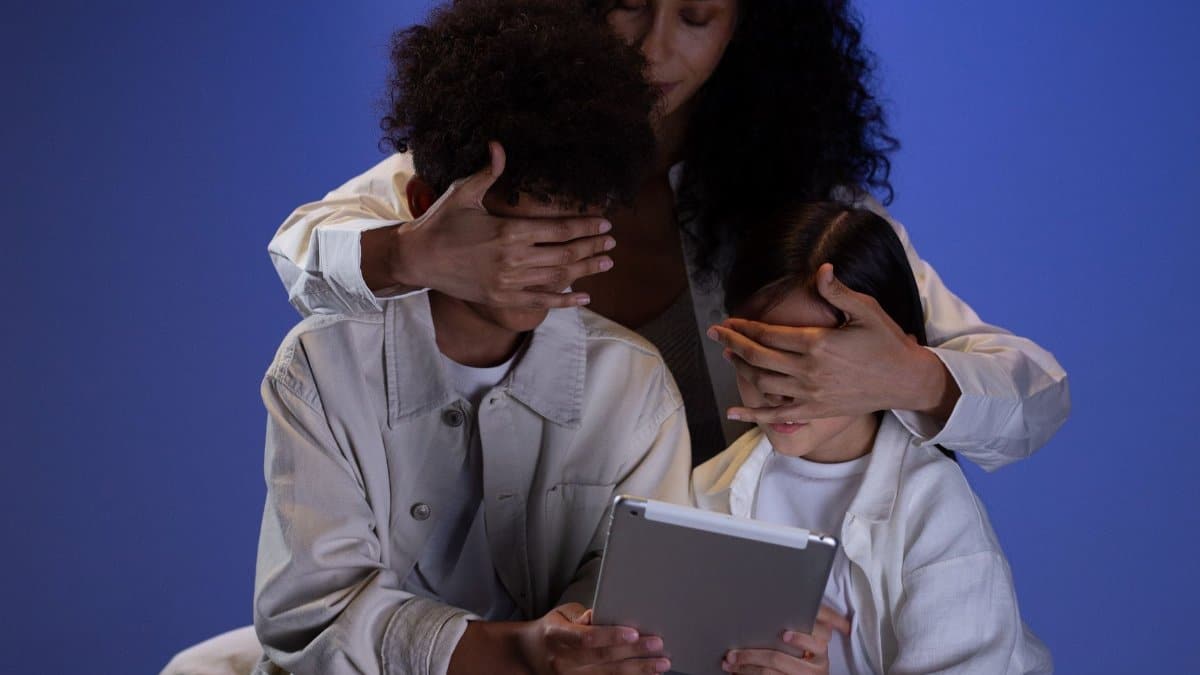 A mother covering her children's eyes while they hold a tablet, illustrating parental control.