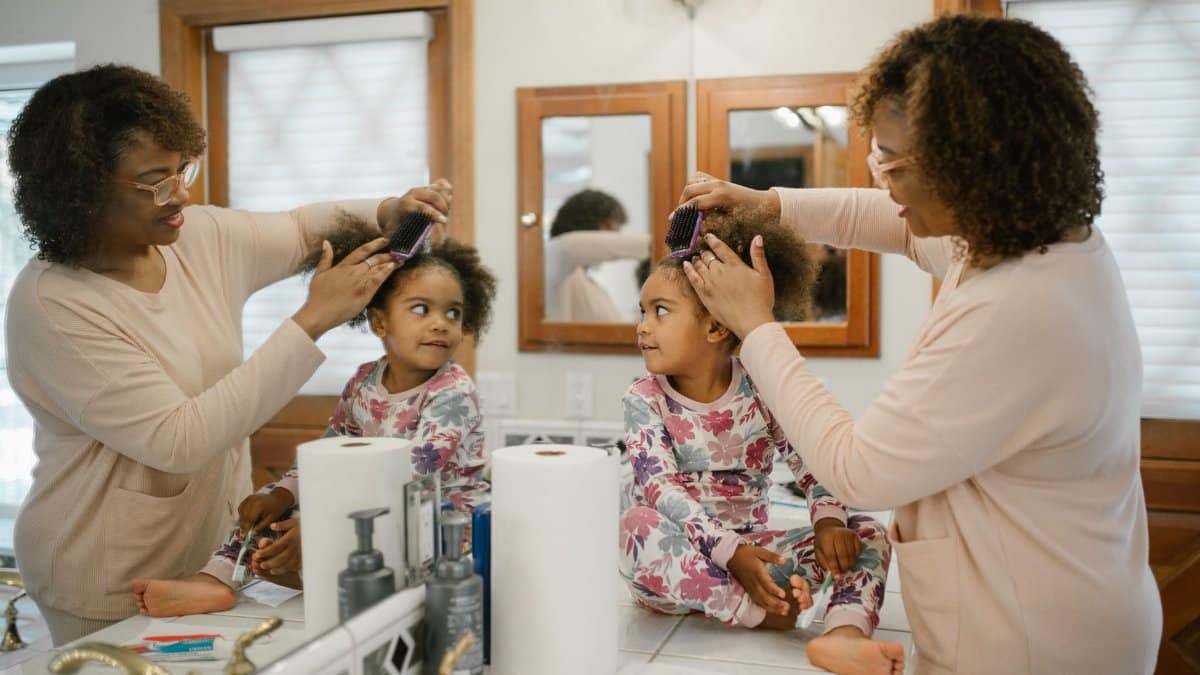 A mother combs her daughter's curly hair in a cozy bathroom setting, showcasing a loving morning routine.