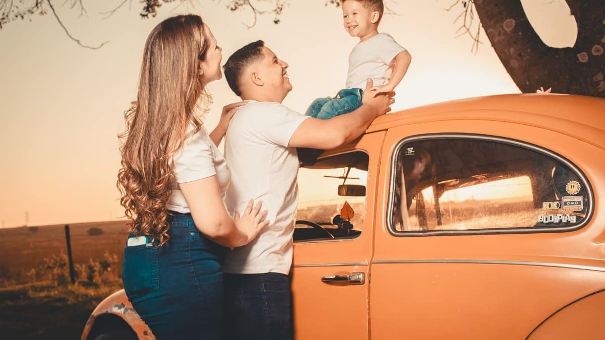 A joyful family enjoying time outdoors by an orange vintage car at sunset.