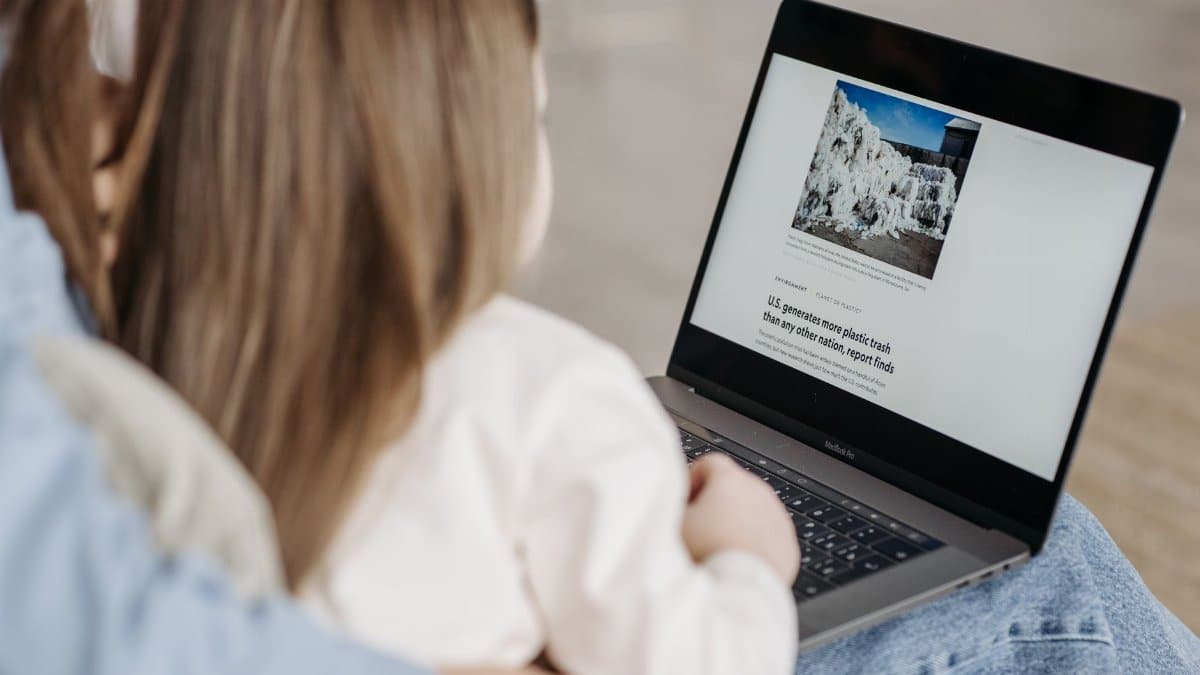 A child sits on an adult's lap, watching a laptop screen with educational content.