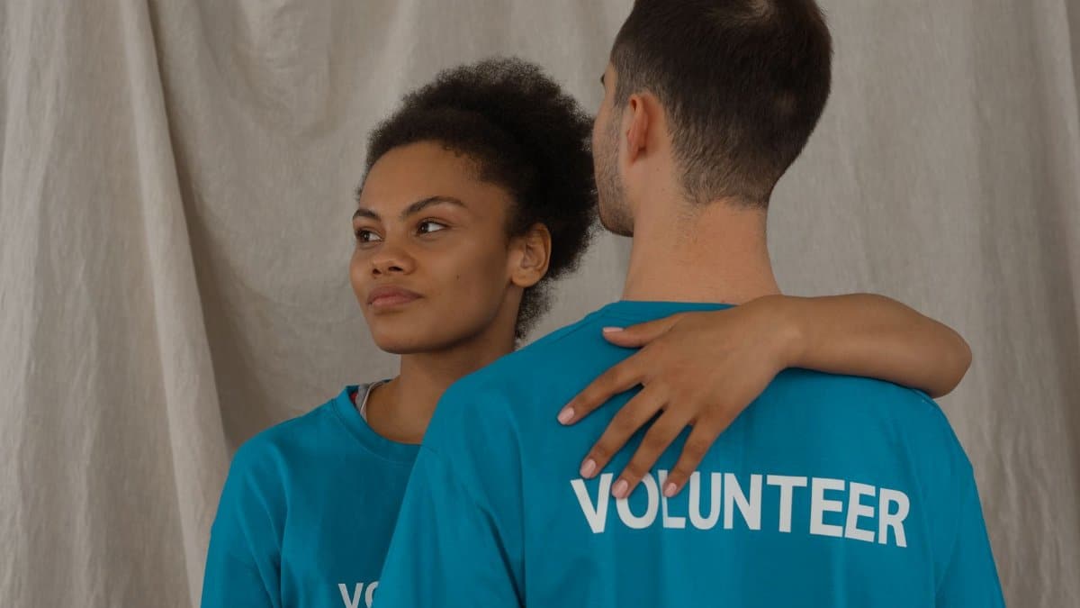 Two volunteers in blue shirts share a supportive embrace indoors, symbolizing community support.