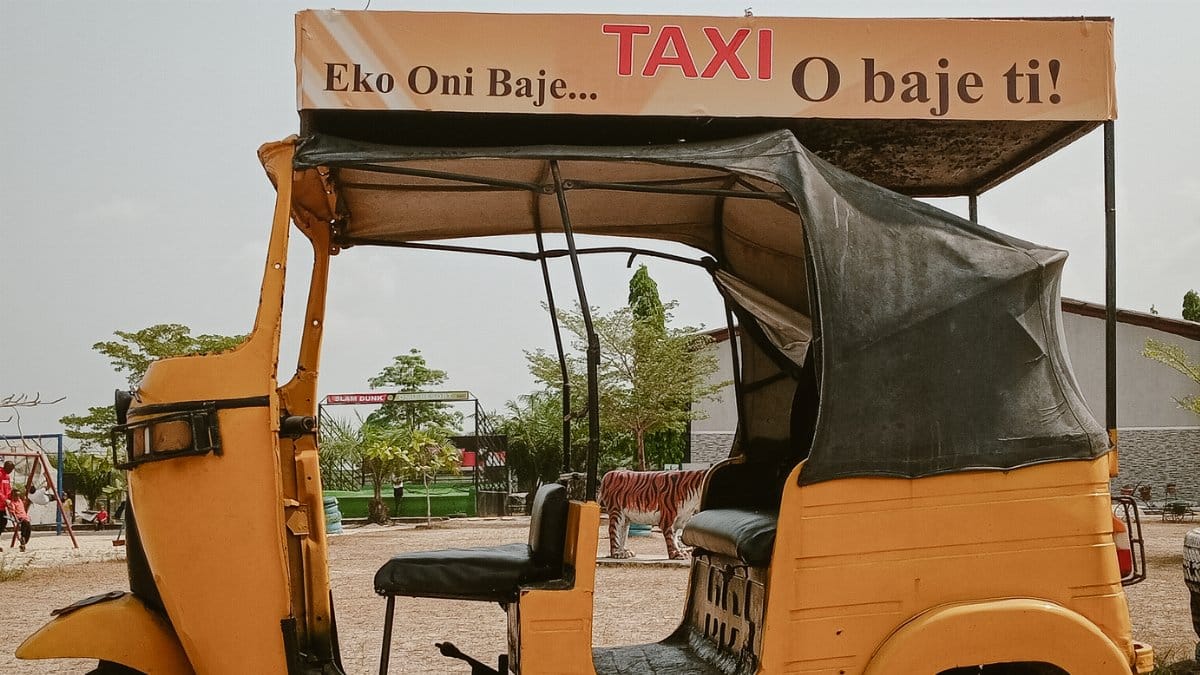 A traditional yellow tuk tuk taxi parked outdoors in a Nigerian setting, showcasing local culture.