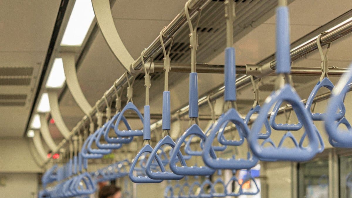 Interior of a public transit train with focus on blue handrails and blurred passengers.