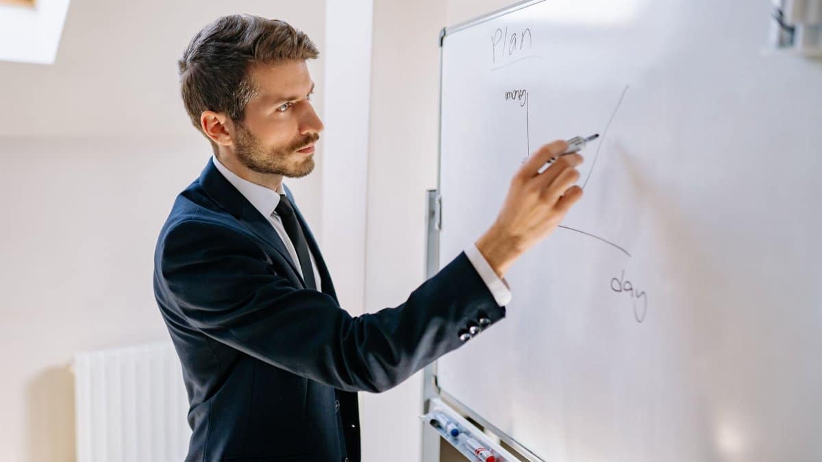 Executive in suit writing on whiteboard, explaining business graph.