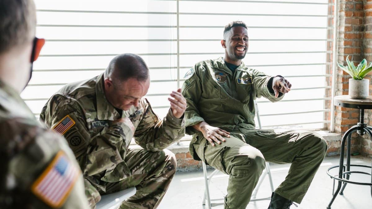 Military veterans laughing together during a supportive group therapy session indoors.