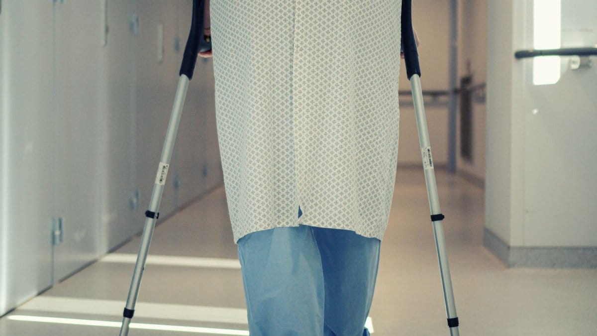 A senior patient using crutches to walk down a hospital corridor, symbolizing recovery and mobility assistance.