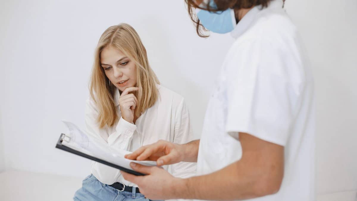 A doctor in a face mask discusses diagnosis with a patient in a clinic setting.