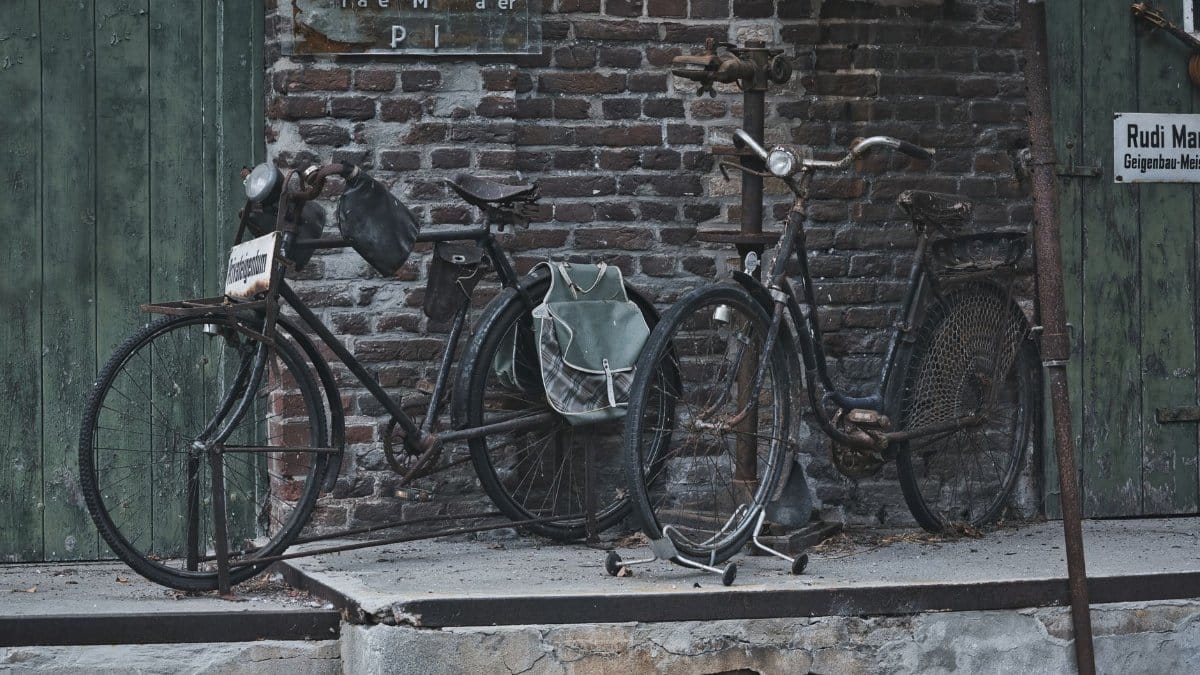 Old, weathered bicycles with rust stand against a rustic brick wall, evoking nostalgia.