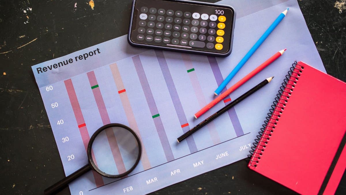 Flat lay of revenue report with a calculator, pencils, and notebook.
