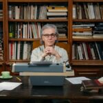 Senior man with typewriter in library, embodying wisdom and literary passion.