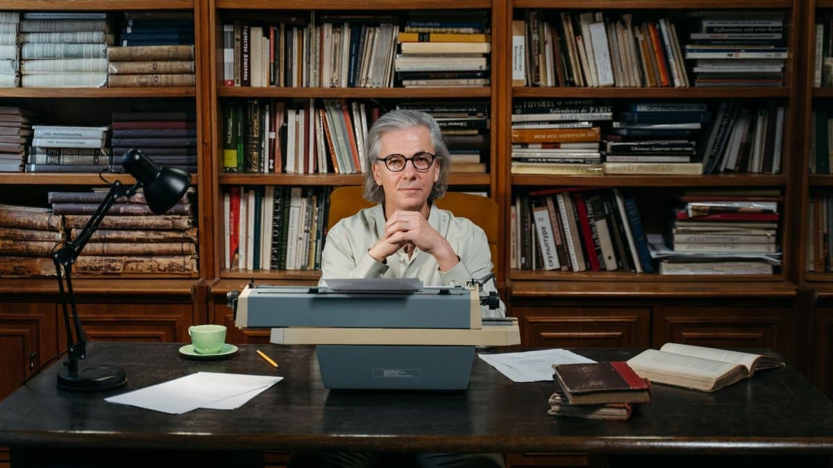 Senior man with typewriter in library, embodying wisdom and literary passion.