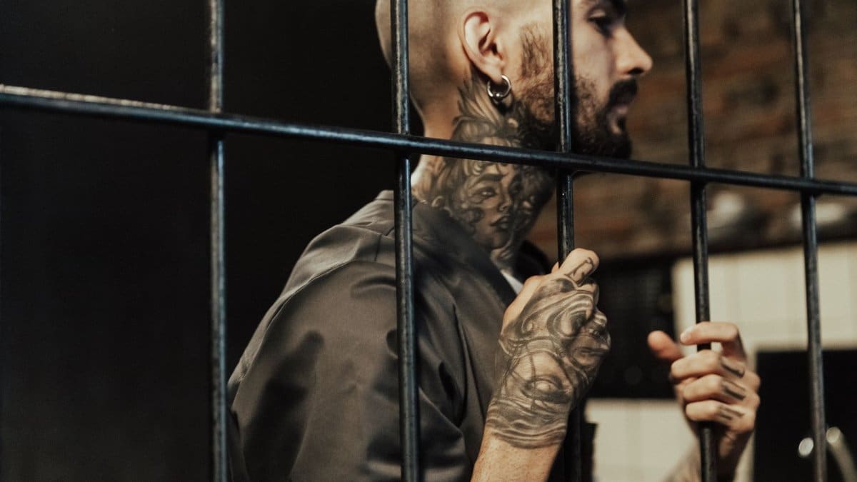 A tattooed man behind prison bars, contemplating life inside a penitentiary.