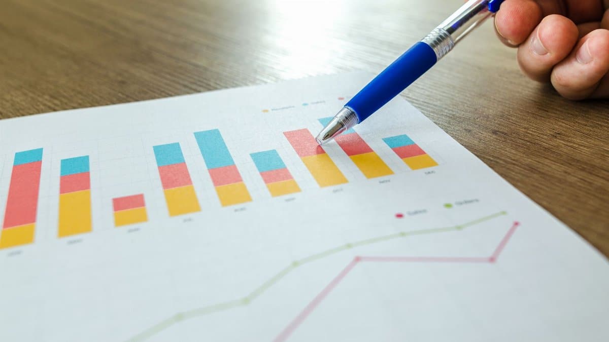 Detailed close-up of a hand pointing at colorful charts with a blue pen on wooden surface.