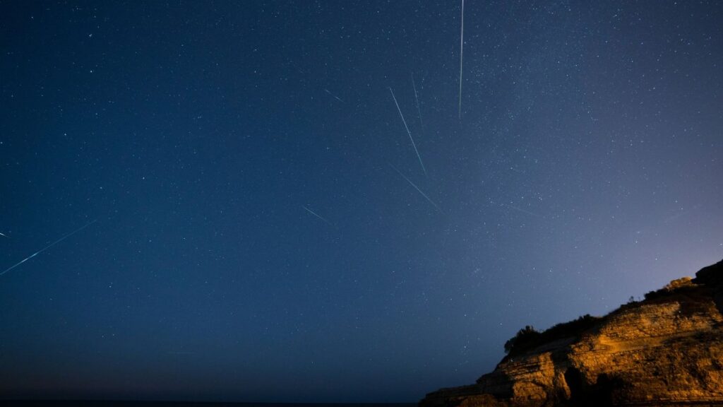 Beautiful starry sky with meteors streaking over a rocky cliff at night.