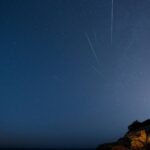 Beautiful starry sky with meteors streaking over a rocky cliff at night.