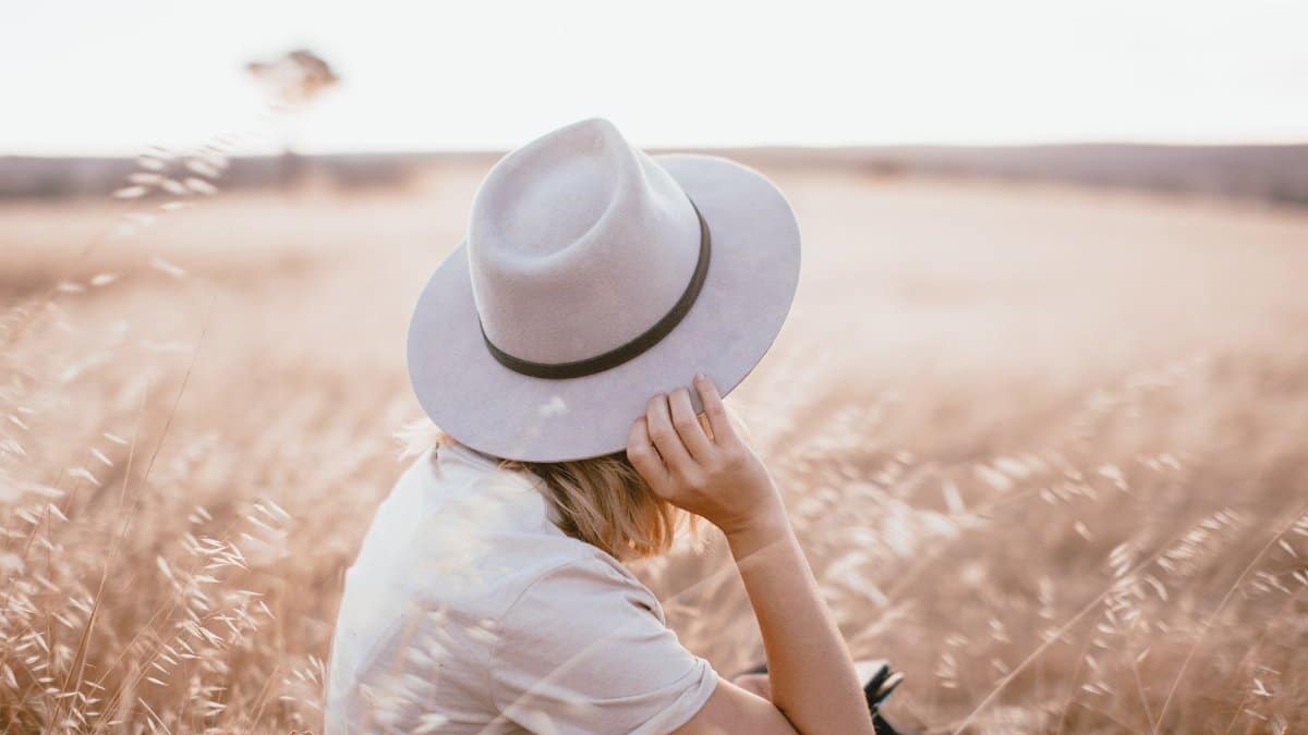 A woman with a gray hat sits in a serene wheat field under natural light.