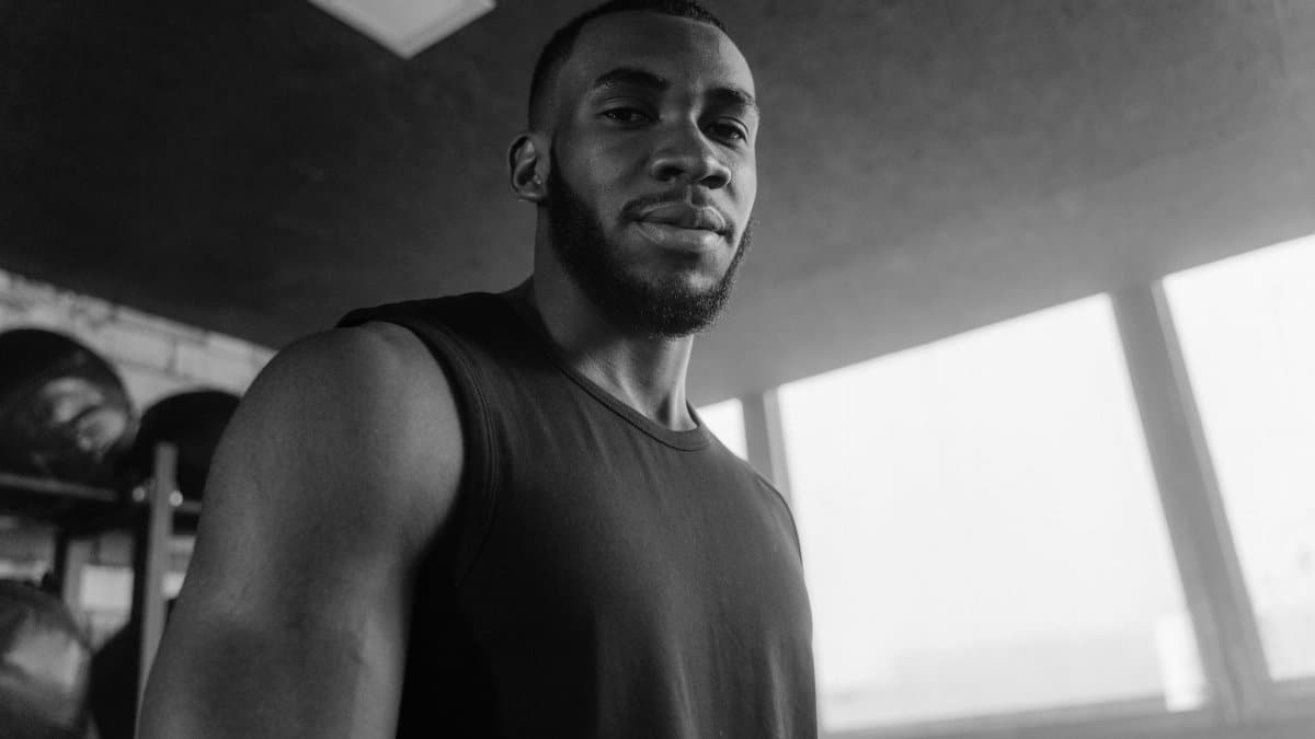 Grayscale photo of a strong man in a gym, wearing a tank top, looking confident.