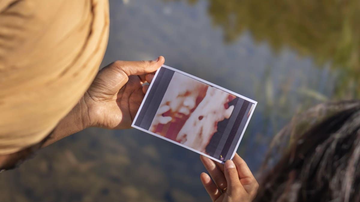 A close-up shot of two individuals examining a blurred photograph near a body of water.