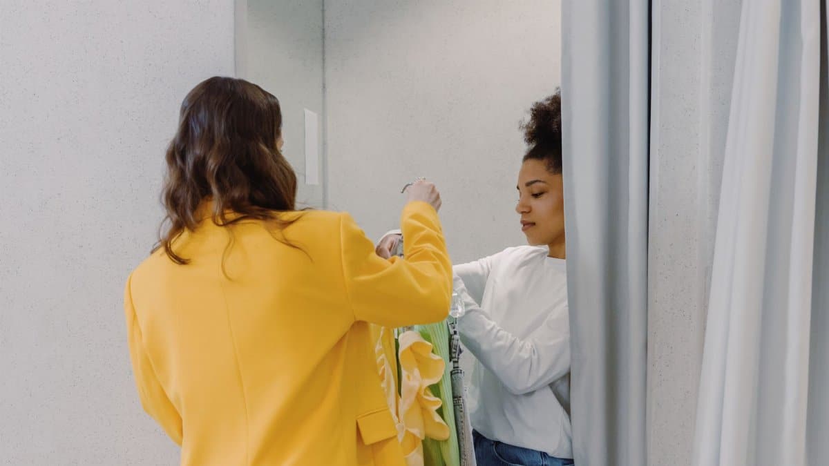 A personal stylist helps a client with clothing choices in a fitting room, focusing on fashion styling.