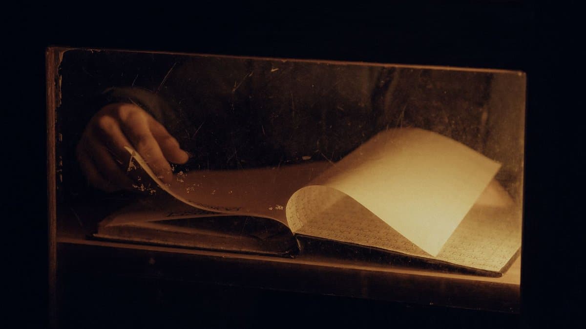 A warm, intimate close-up of hands turning pages in a book under soft lighting, creating a reflective mood.