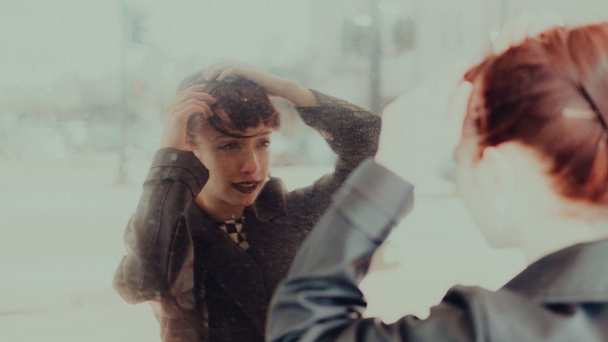 A woman adjusting her hair in a mirror, reflected with a soft and moody ambiance.