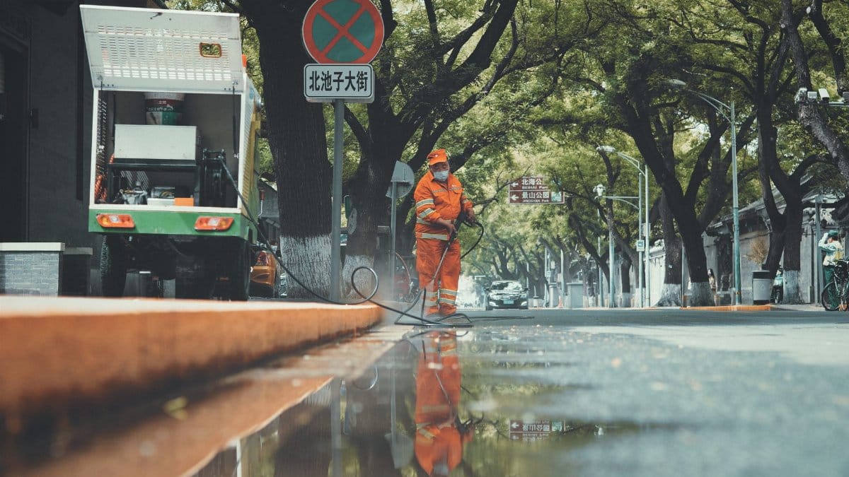 Street cleaner using power spray on a wet Beijing street with reflections.