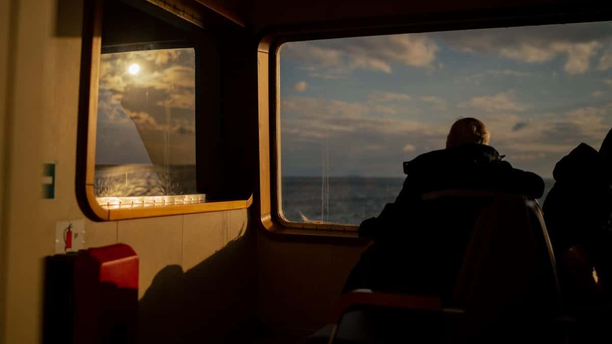 A person gazes out the ferry window at the sea during sunset, creating a serene mood.