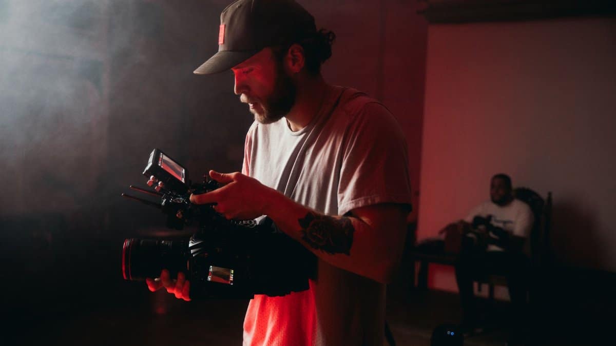 Professional cinematographer operating a camera indoors with dramatic lighting.