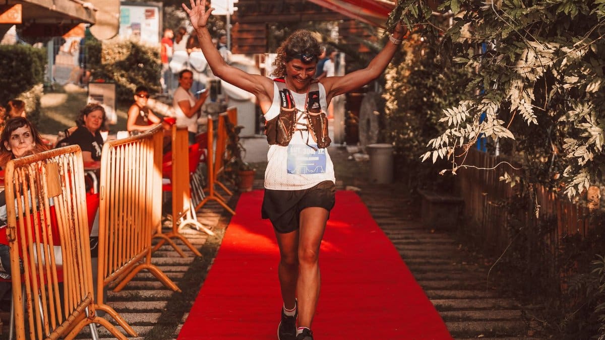 Smiling woman crossing the finish line in an urban race, arms raised in victory.