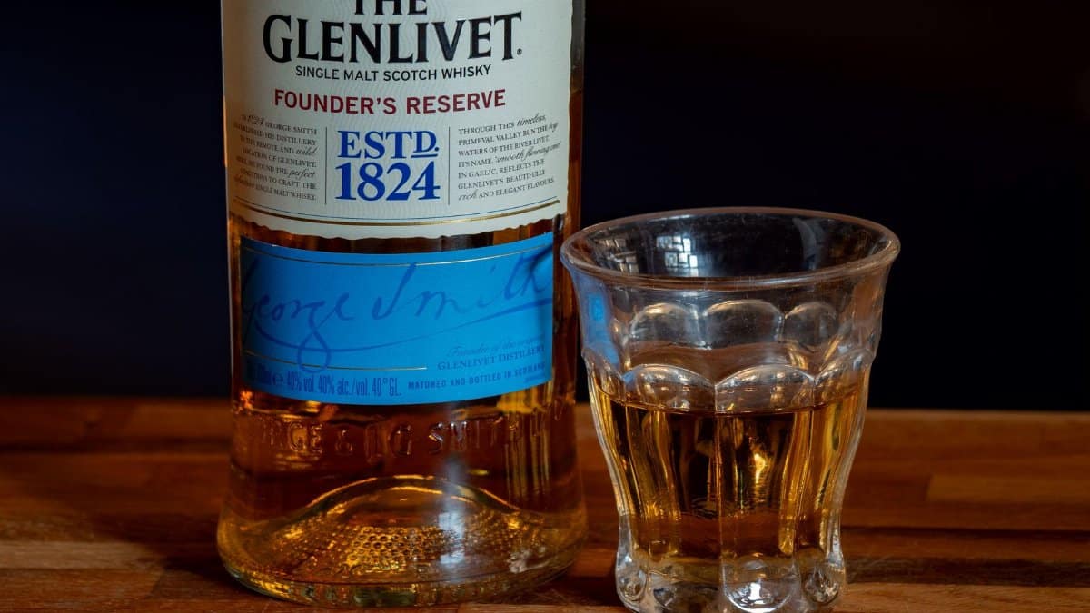 Close-up of The Glenlivet Founder’s Reserve whisky with a glass on a wooden surface.