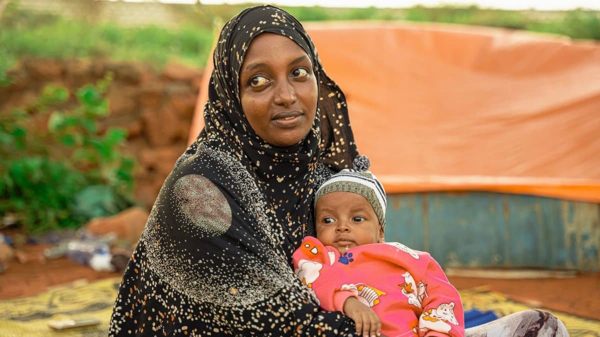 A mother holds her baby outdoors, conveying contentment and love.