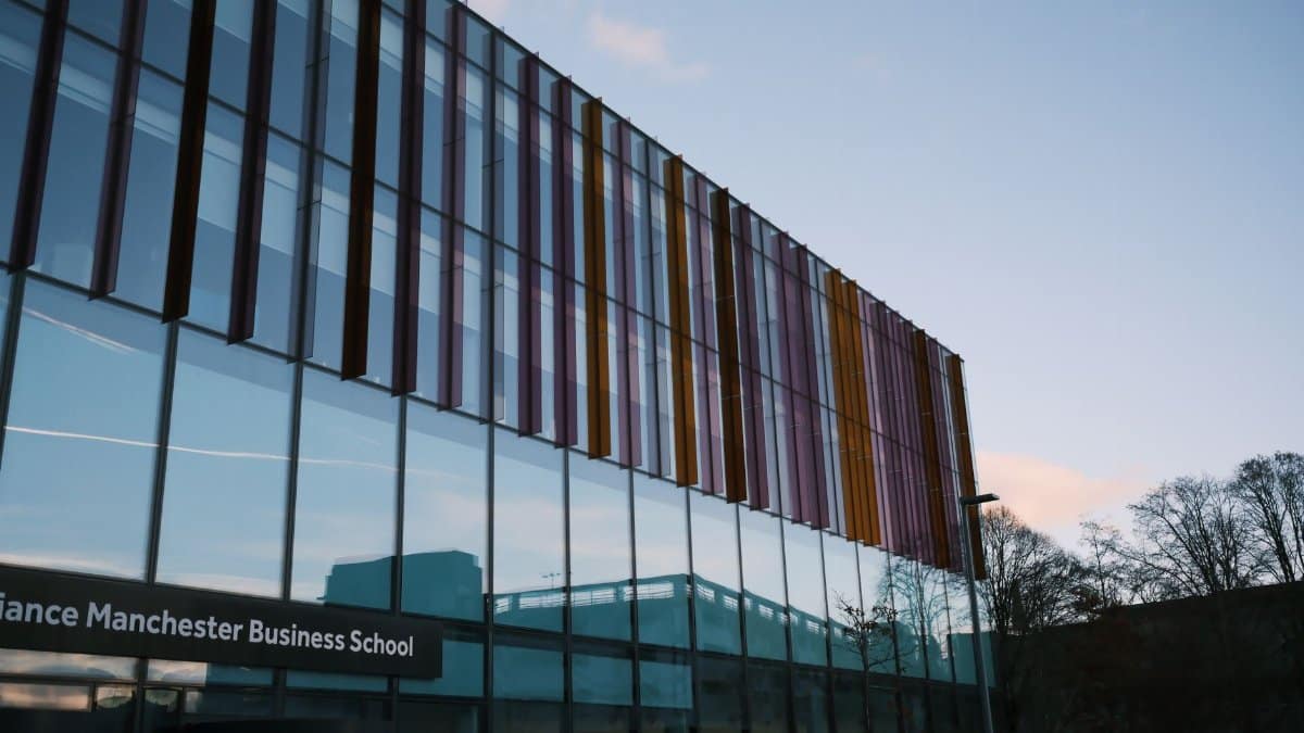 Modern architecture of Alliance Manchester Business School reflecting in glass facade at dusk.