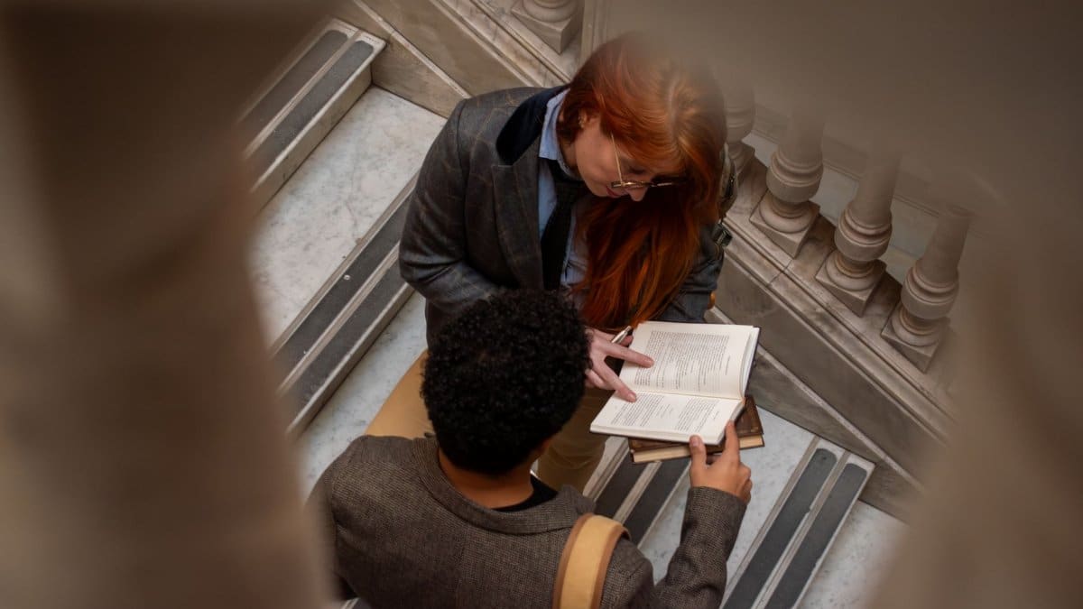 Two students engaged in conversation while reading a book on an indoor staircase.