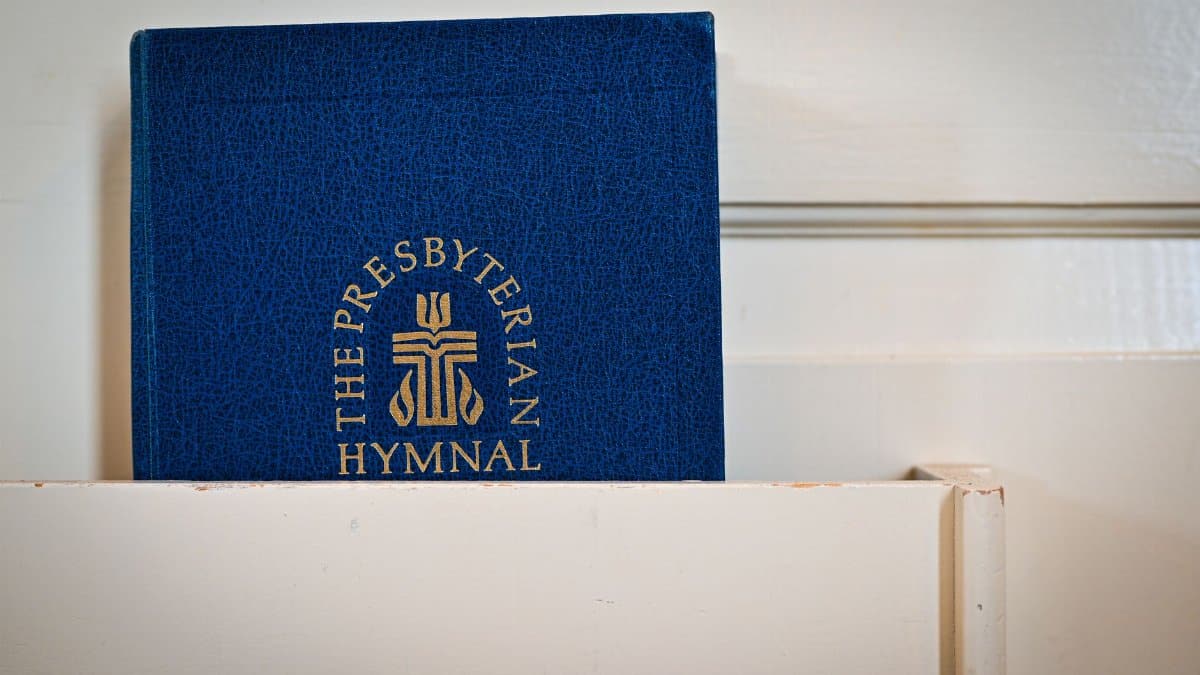 Detail of a blue Presbyterian hymnal resting on a church pew indoors.