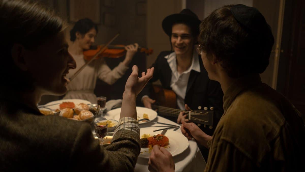 A joyous Jewish family gathering with music, featuring guitar and violin, during a festive meal indoors.