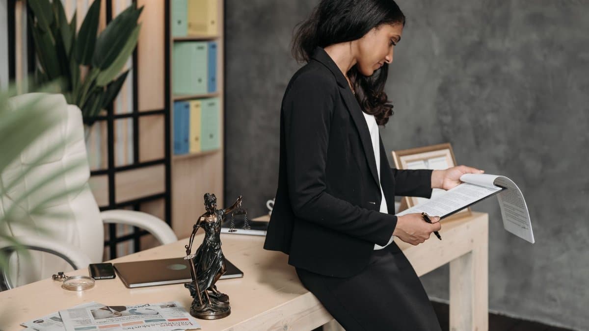 A professional woman in a business suit reviews legal documents at her office desk.