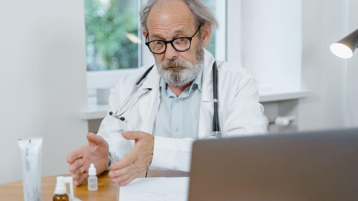 An elderly doctor in a white coat conducting an online medical consultation, focusing attentively.