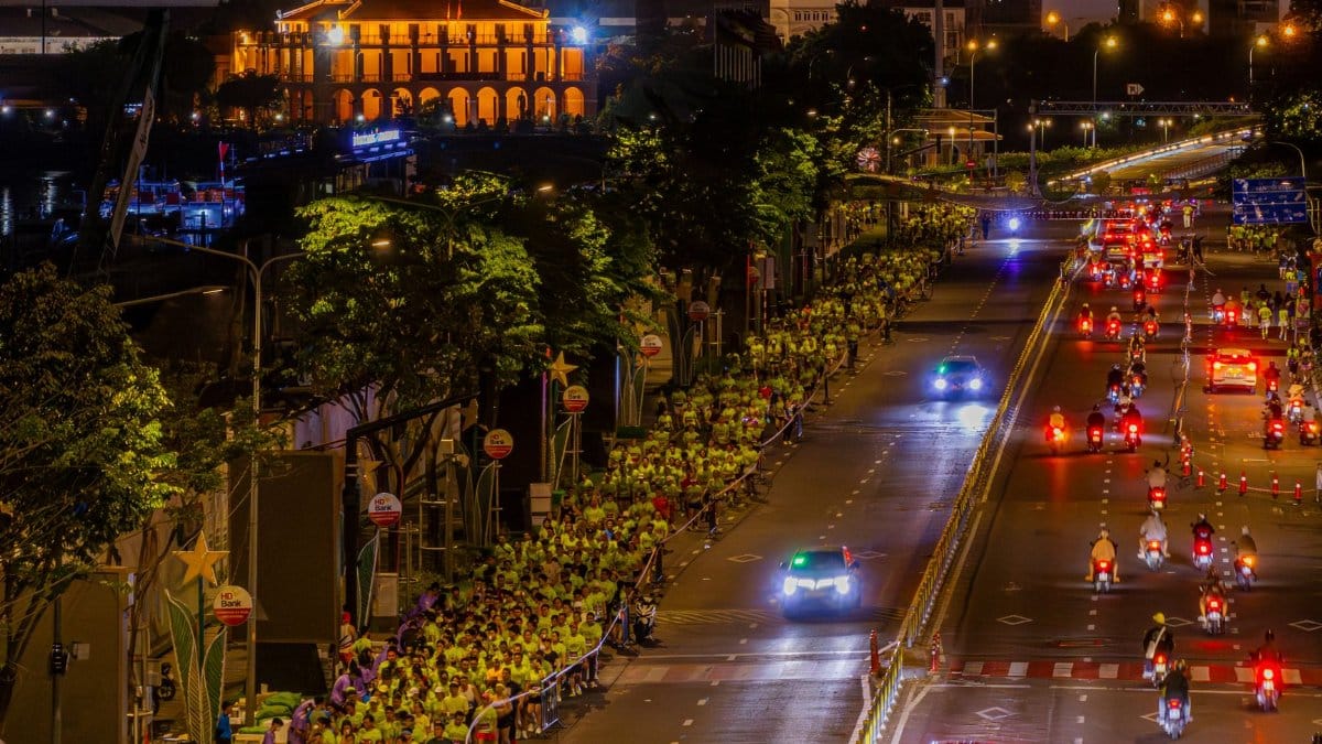 Night marathon with participants and vehicles in a lively city street under illuminated skyline.