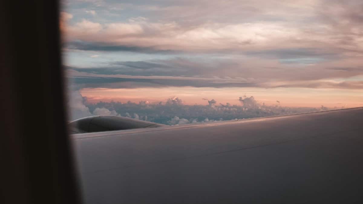 View from airplane window showing wing and serene sunset skies above clouds.