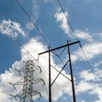 High-voltage power lines and towers set against a vibrant blue sky with scattered clouds.