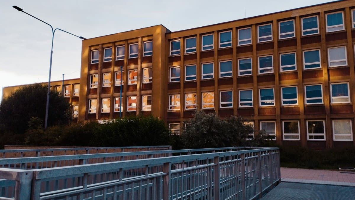 A modern school building facade illuminated at twilight with a pedestrian walkway in the foreground.