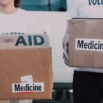 Volunteers holding boxes labeled 'AID' and 'Medicine', preparing donations.