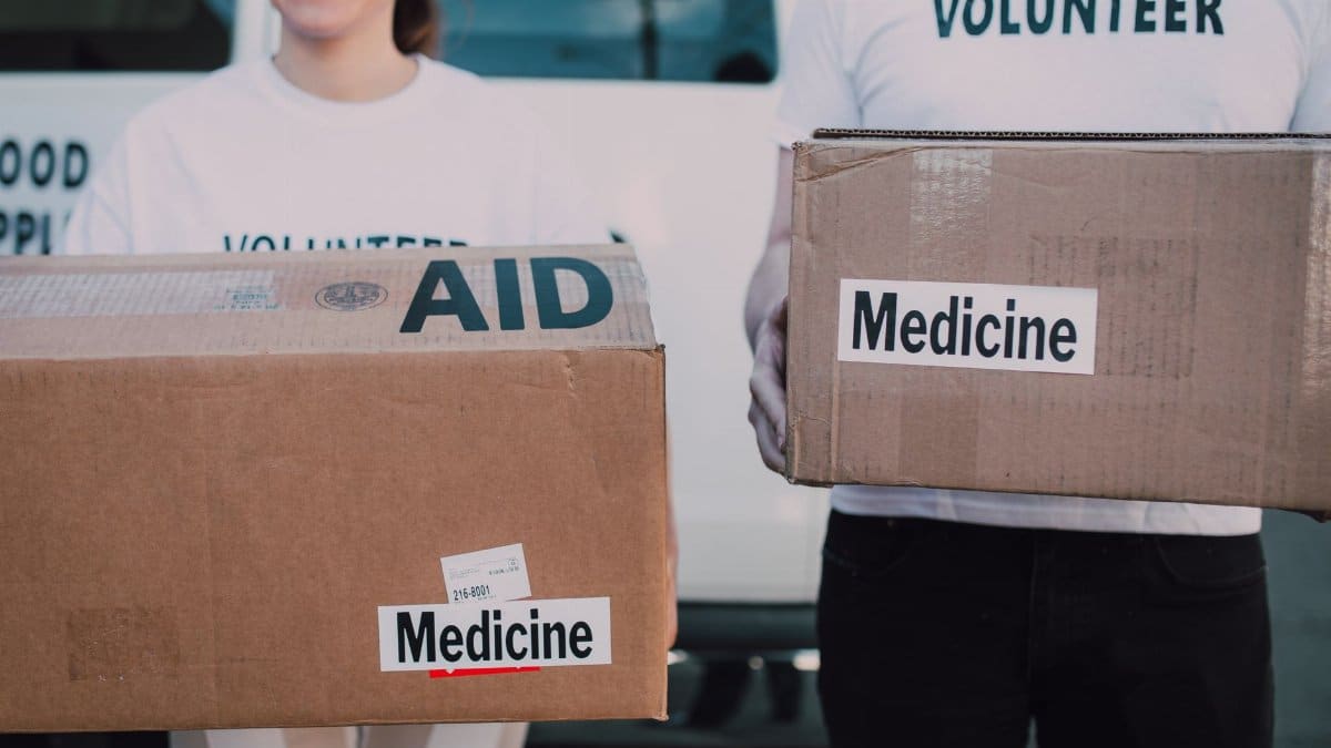 Volunteers holding boxes labeled 'AID' and 'Medicine', preparing donations.