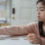 Young Asian girl with Down Syndrome engaged in a game indoors, wearing a pink sweater.