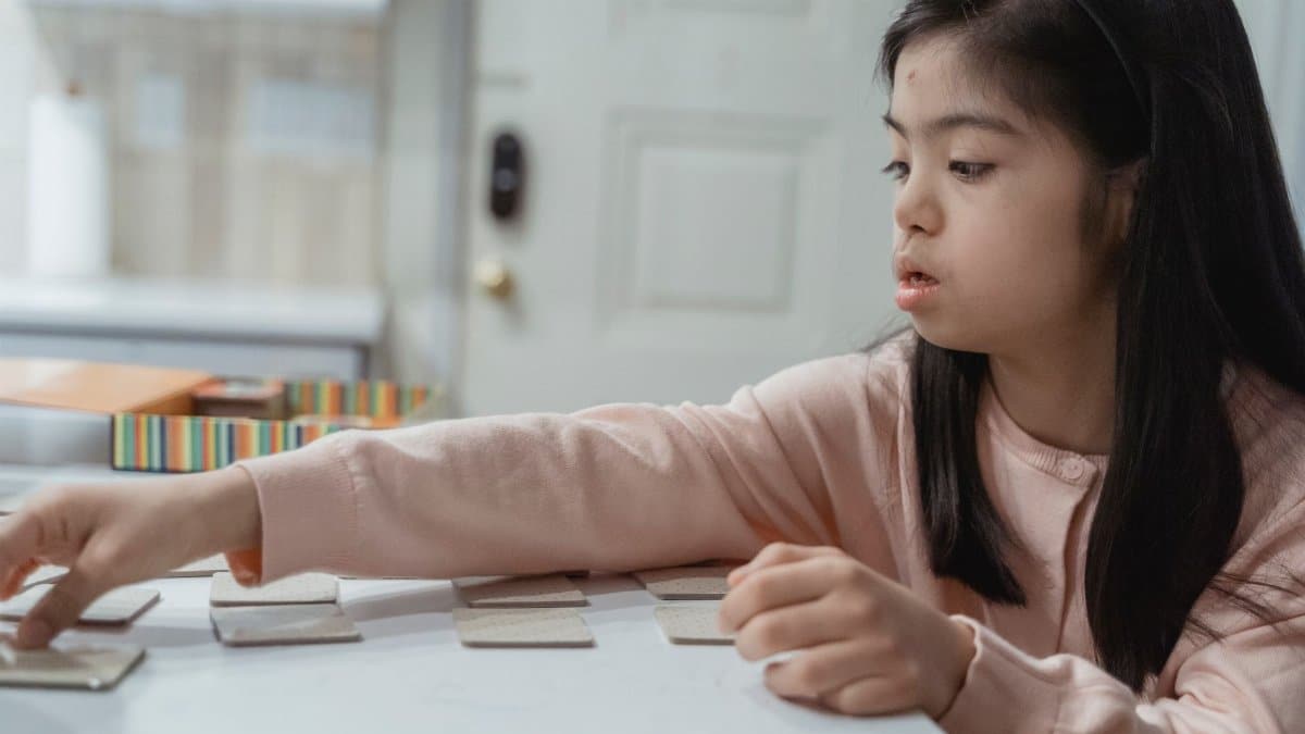 Young Asian girl with Down Syndrome engaged in a game indoors, wearing a pink sweater.