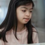 A young girl with Down syndrome playing attentively at a desk indoors. Bright and warm ambiance.