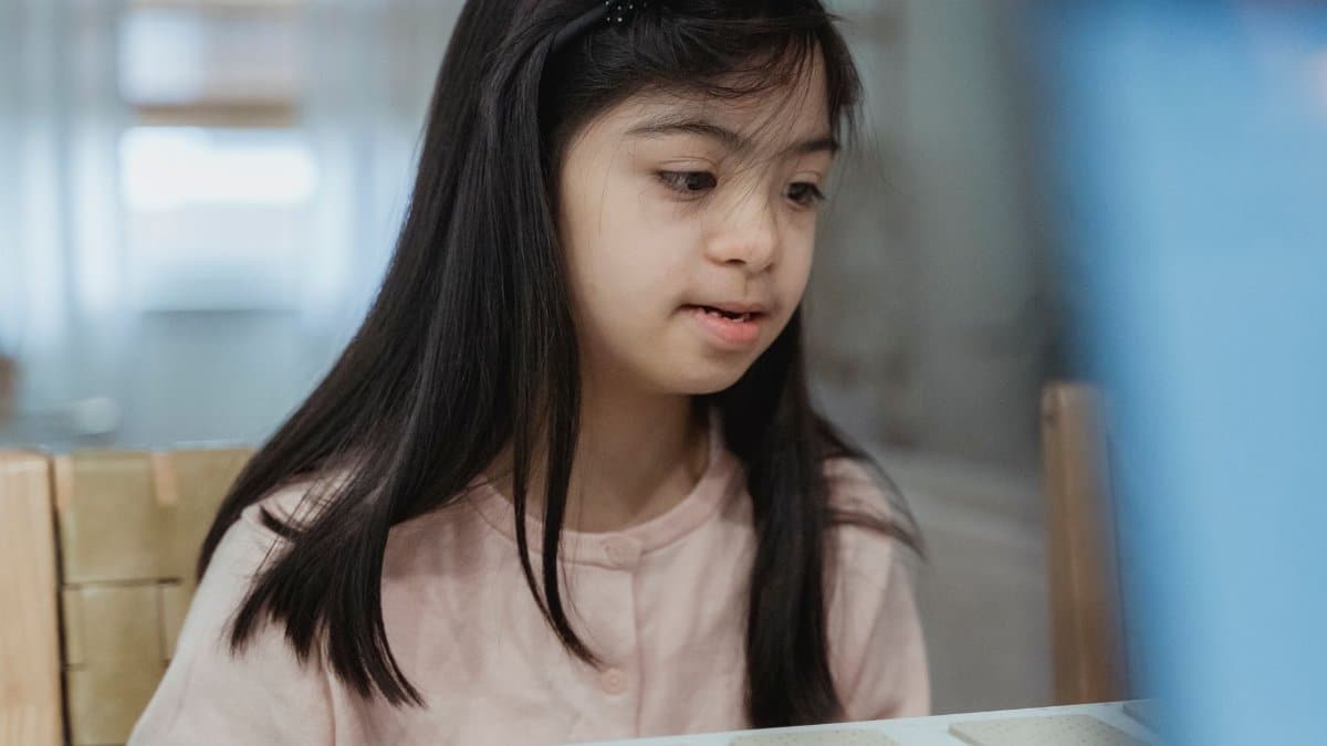 A young girl with Down syndrome playing attentively at a desk indoors. Bright and warm ambiance.